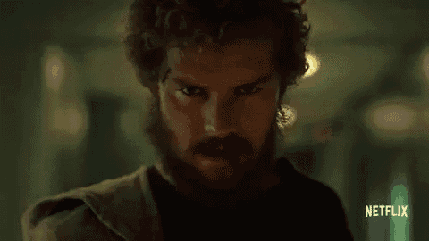 a man with a beard and curly hair is standing in a dark room and looking at the camera .