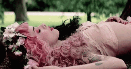 a woman with pink hair and a flower crown laying on the ground .