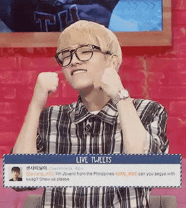 a young man wearing glasses and a plaid shirt is standing in front of a live tweet