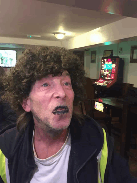 a man with a wig on his head is sitting in front of an arcade game
