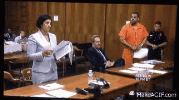 a man in a orange jumpsuit is standing in front of a woman holding papers in a courtroom