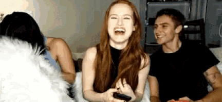 a man and a woman are sitting on a bed laughing and playing a video game .