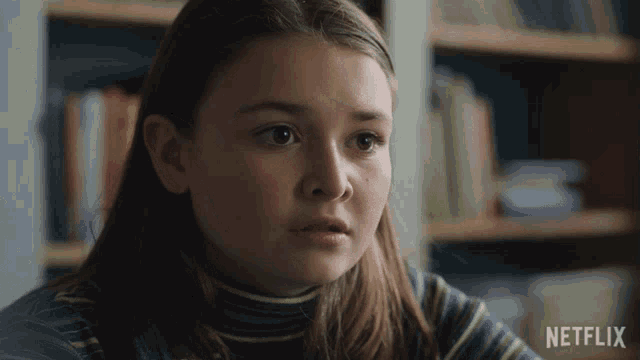 a girl in a striped shirt is sitting in front of a shelf with netflix written on it