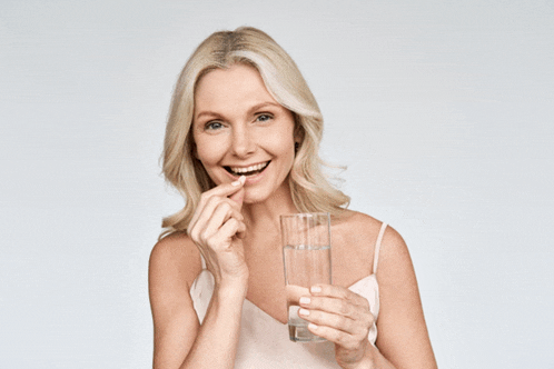 a woman is holding a glass of water and a pill in her mouth