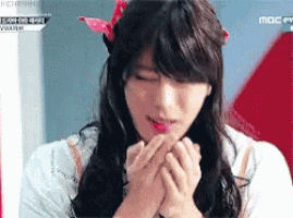 a woman with long hair and a pink bow on her head is holding her hands to her face .