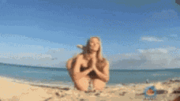 a woman in a bikini is kneeling on a sandy beach near the ocean .