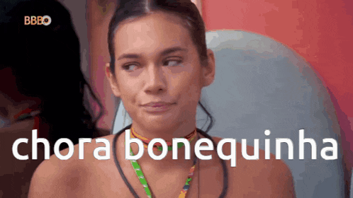 a woman is sitting in front of a screen that says " chora bonequinha "