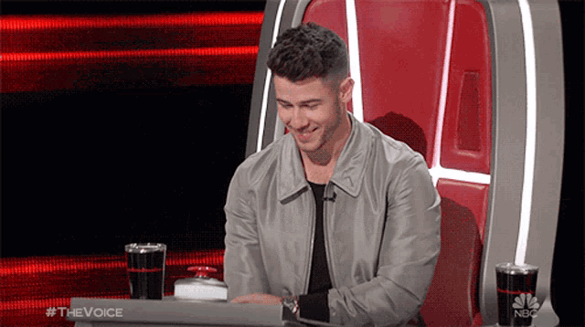 a man is sitting in a chair with a laptop on his lap and the words #thevoice are on the screen behind him