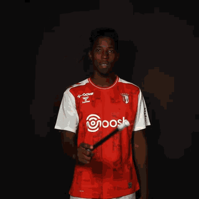 a man in a red and white shirt is holding a stick in his right hand .