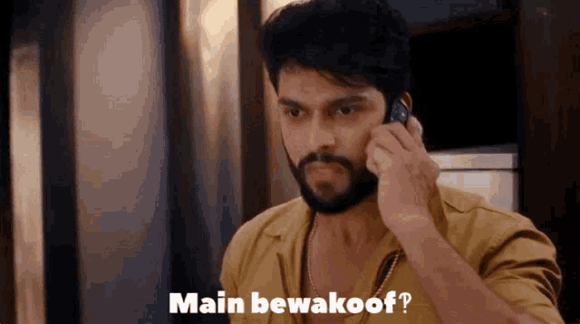 a man with a beard is talking on a cell phone with the words main bewakoor written on the bottom