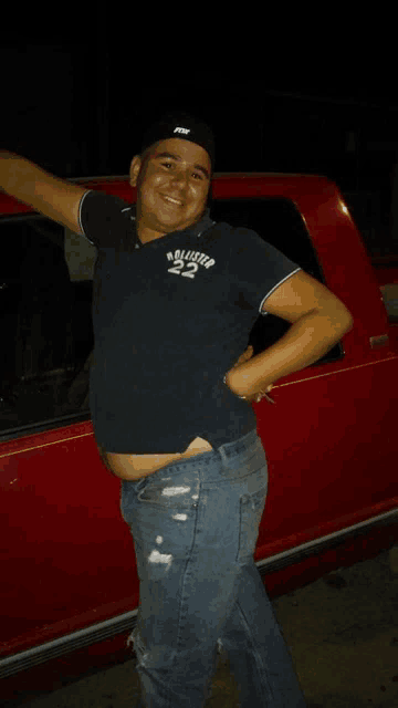 a man wearing a hollister shirt is standing in front of a red car