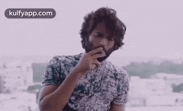 a man with a beard is smoking a cigarette while wearing a t-shirt .