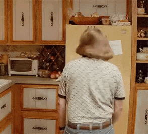 a man in a striped shirt is standing in a kitchen near a refrigerator