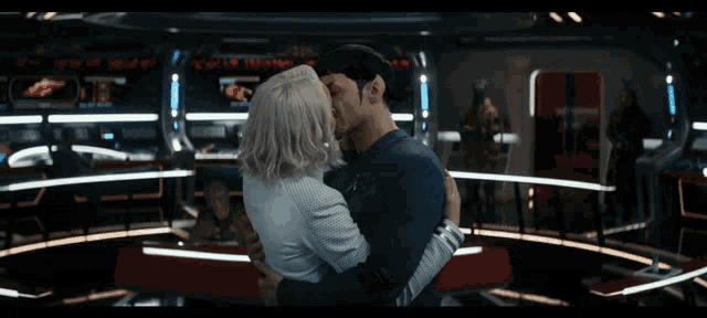 a man and woman are kissing in a room with a star trek logo on their shirt