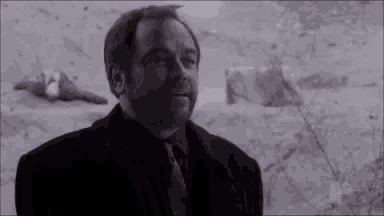 a man in a black suit and tie is standing in front of a snowy field .