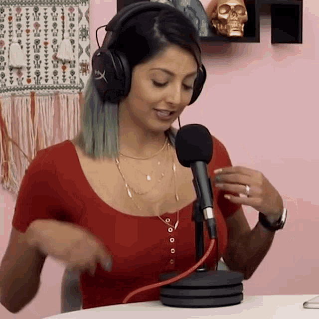 a woman wearing headphones and a red shirt is sitting in front of a microphone