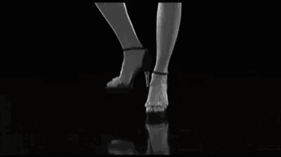 a black and white photo of a woman 's feet surrounded by shoes