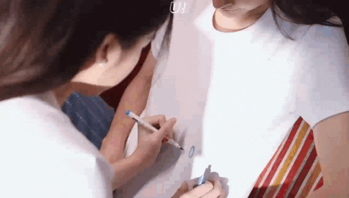 two women are sitting at a table writing on a white shirt .