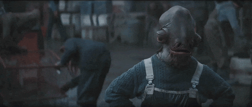 a man wearing overalls and a mask is standing in front of a group of people .