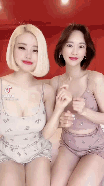 two women are sitting next to each other on a bed and smiling for the camera .