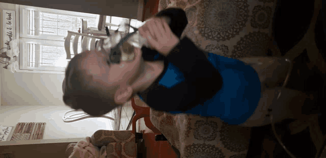 a boy in a blue shirt is drinking from a glass
