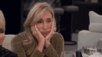 a woman is sitting at a table with her hands on her face and a glass of wine .