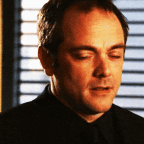 a man in a black suit and tie is looking down with his eyes closed