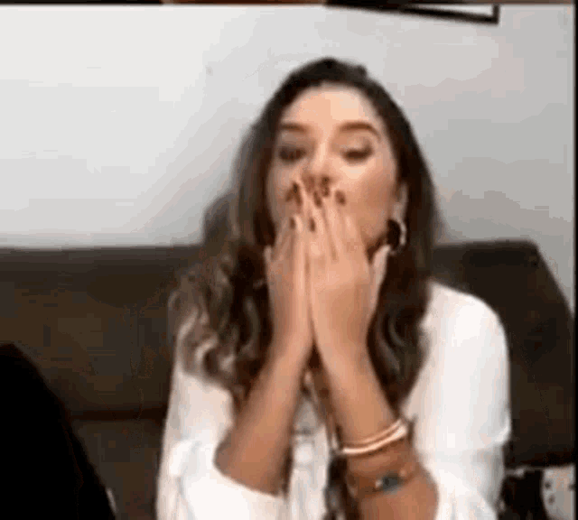 a woman is sitting on a couch with her hands over her mouth .