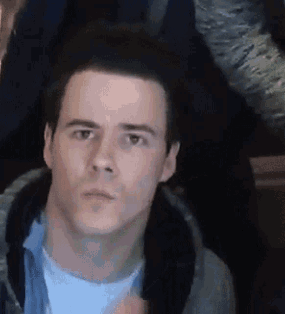 a man wearing a hoodie and a white shirt is looking at the camera with a serious look on his face .