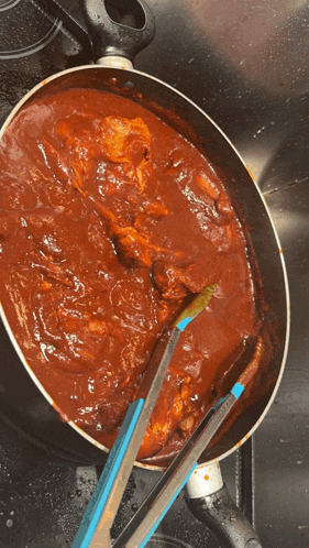 a frying pan filled with red sauce and tongs on a stove top