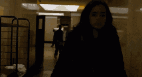 a woman is walking down a hallway with a man in the background .
