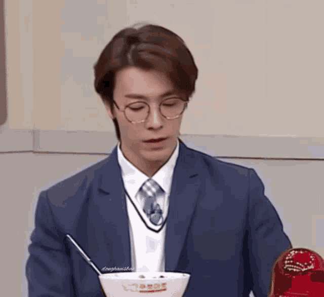a man in a suit and tie is sitting at a table with a bowl of food and a straw .
