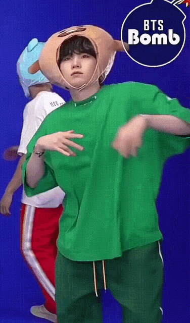 a person wearing a green shirt and a stuffed animal hat is dancing in front of a bts bomb sign