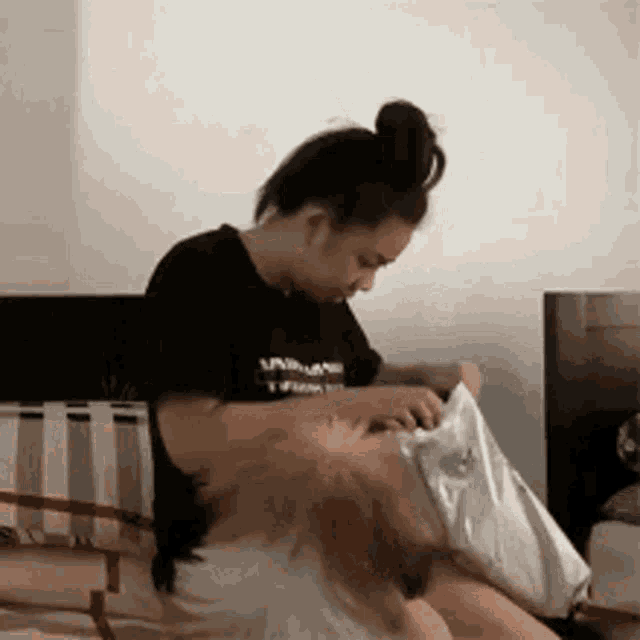a woman in a black t-shirt is sitting on a bed holding a bag .