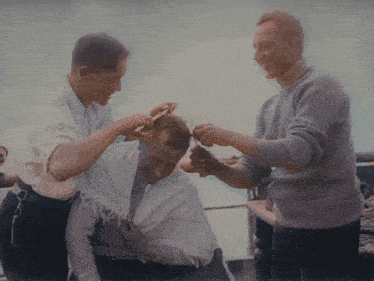 two men are cutting a man 's hair with a pair of scissors