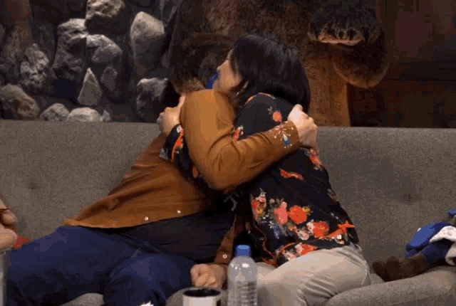 a man and a woman hugging on a couch with a bottle of water in front of them