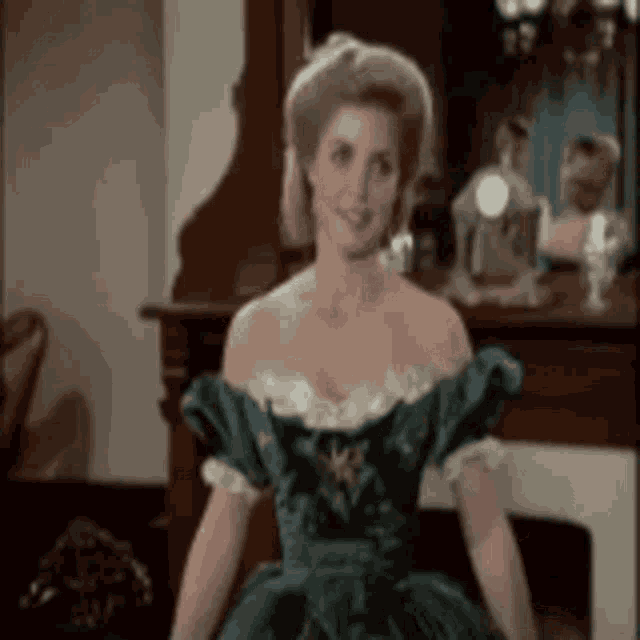 a woman in a green dress is sitting in front of a fireplace .