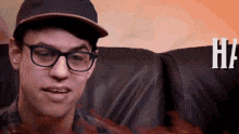a man with glasses and a hat is sitting on a couch .