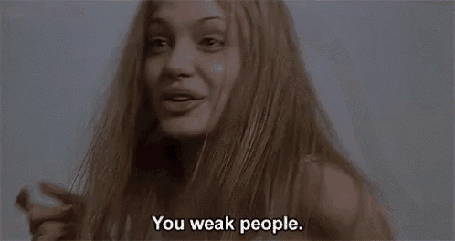 a woman with long blonde hair is standing in front of a wall and says `` you weak people . ''