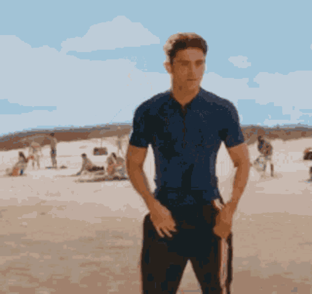 a man in a blue shirt is standing on a sandy beach