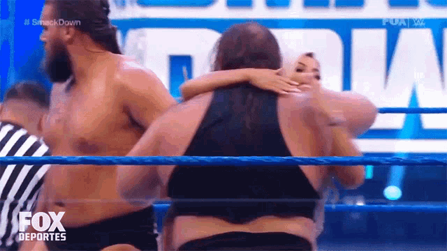 a woman is hugging a man in a wrestling ring while a referee watches .