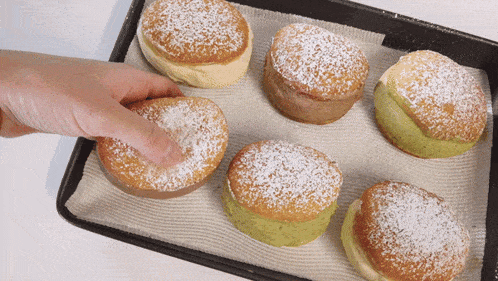 a person reaches for a pastry with powdered sugar on it on a tray