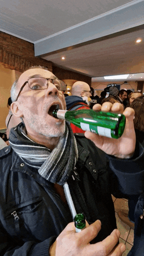 a man wearing glasses is drinking from a green bottle with a white label