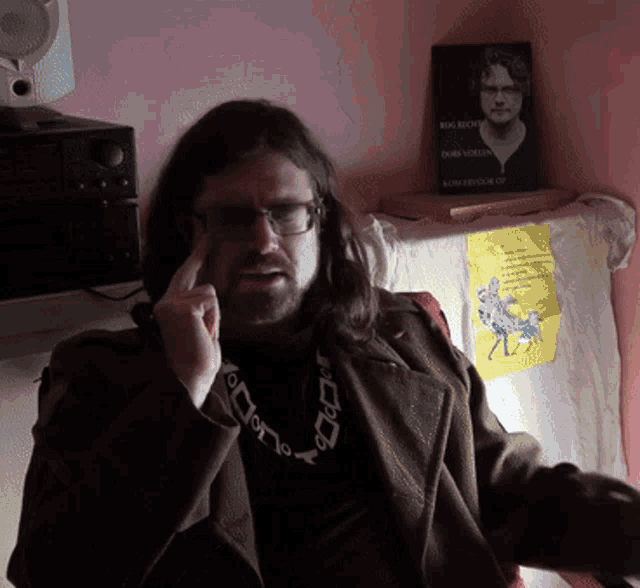 a man wearing glasses and a necklace is sitting in front of a sign that says ' king leondor of '