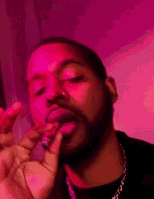 a man is smoking a cigarette in front of a pink background .