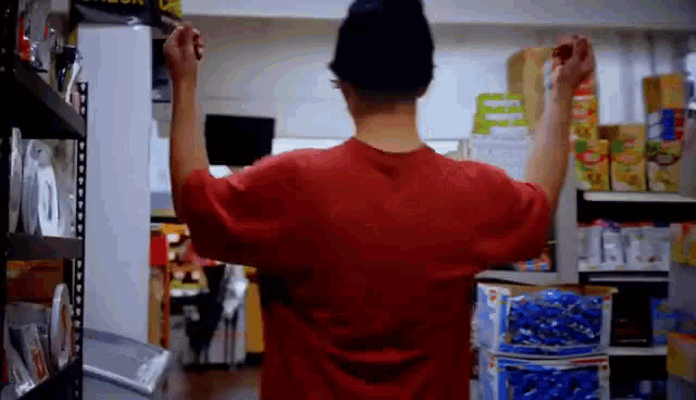 a man in a red shirt is standing in a store with his arms in the air .