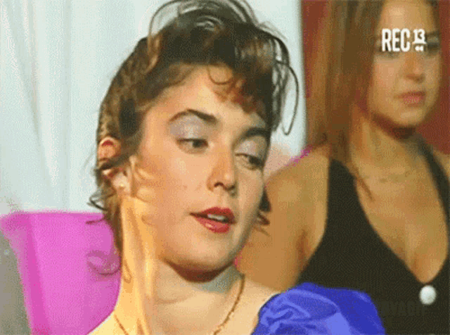 a woman in a blue dress looks at the camera while a woman in a black tank top looks on ..