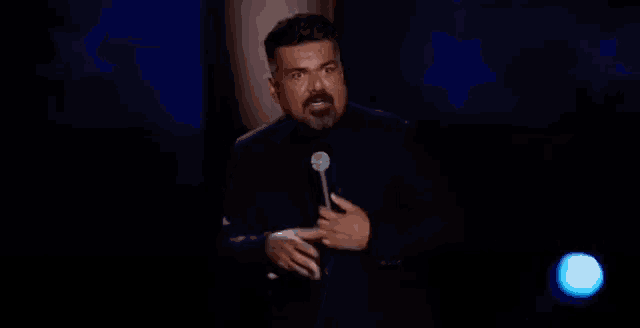 a man with a beard is speaking into a microphone in a dark room
