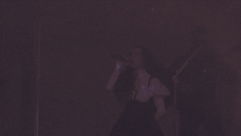 a woman is dancing in front of a microphone and a man is playing a guitar