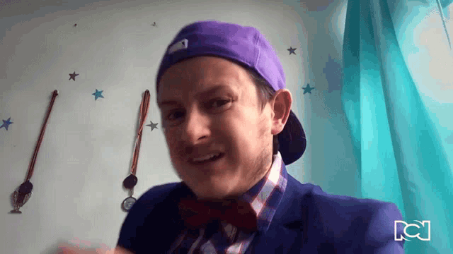 a man wearing a purple hat and a bow tie stands in front of a wall with wands and stars on it
